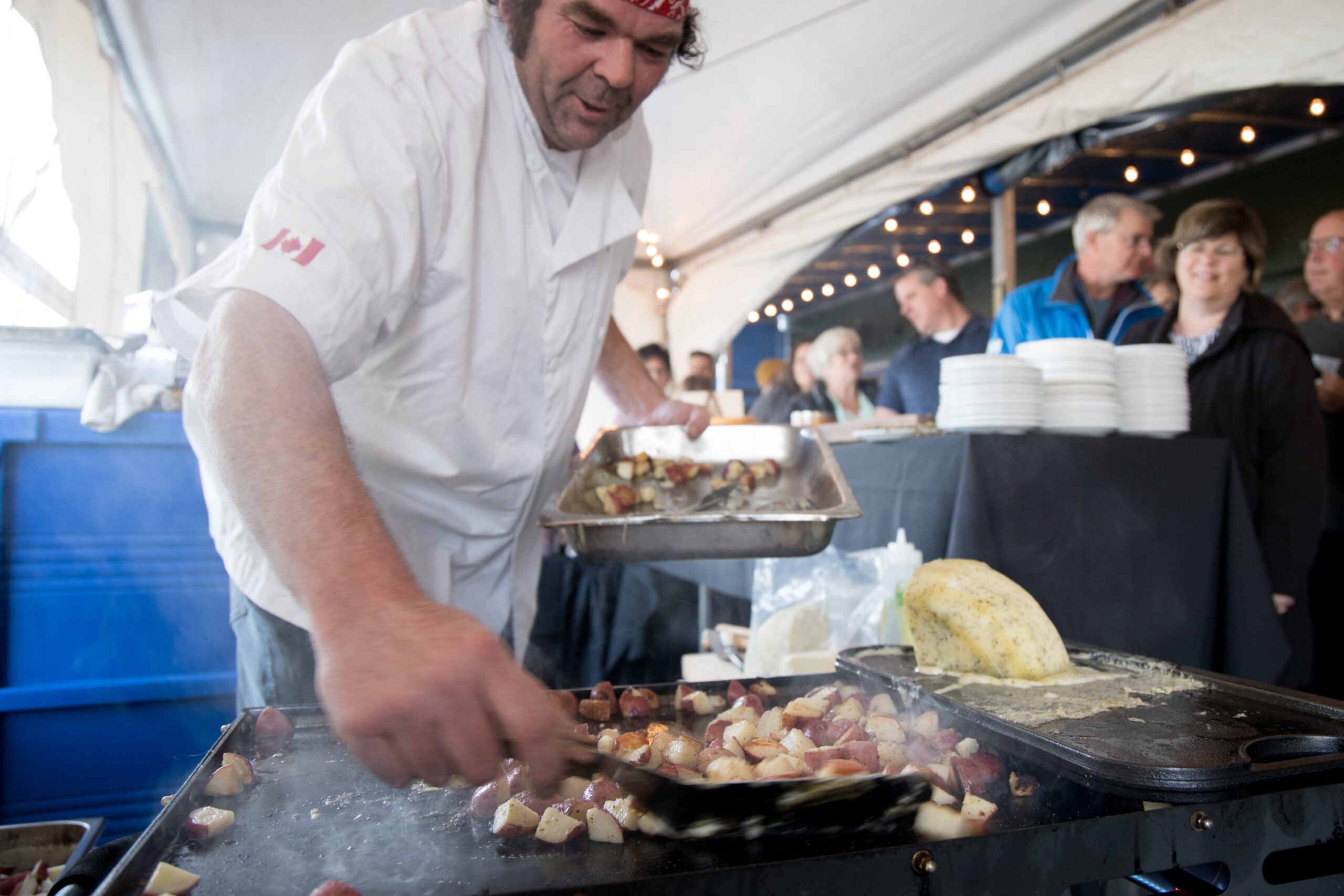 a photo of a chef frying potatoes at an outdoor event