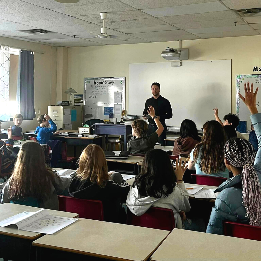 photo of students in a classroom raising their hands